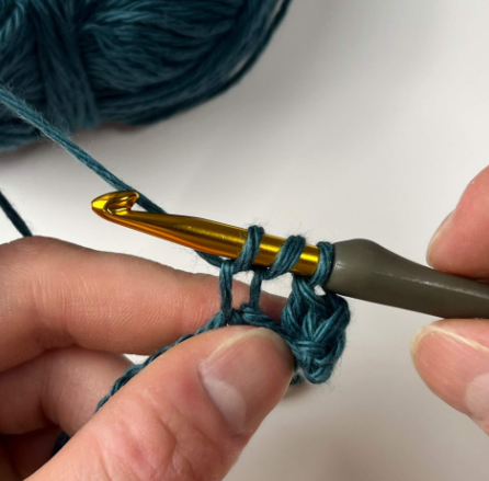 Crochet hook with two loops remaining, mid-way through a double crochet stitch